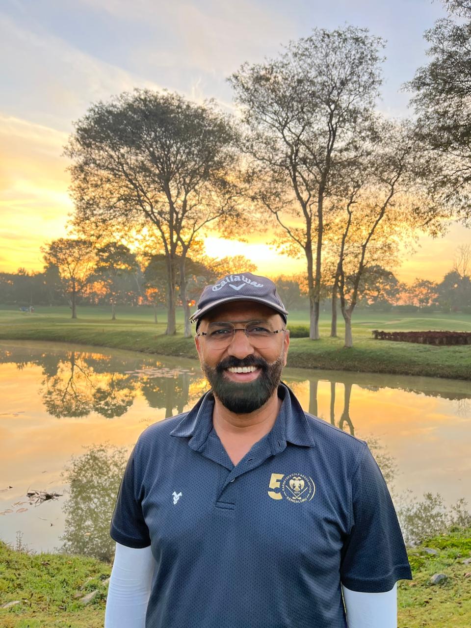 Govind Raj smiling on a golf course at sunrise beside a lake